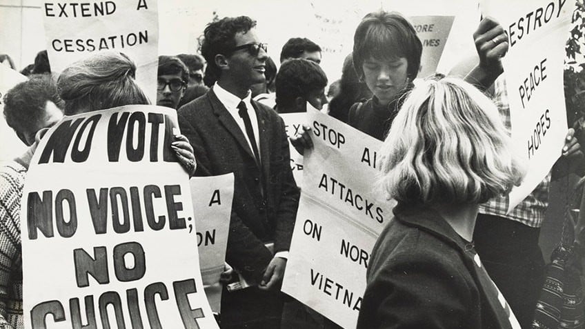 black and white photograph of men and women with posters reading No vote no voice; no choice and Stop all attacks on North Vietnam