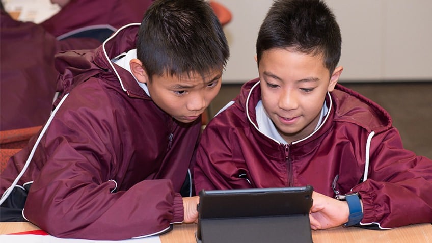 Two schoolboys in maroon jackets looking at a tablet