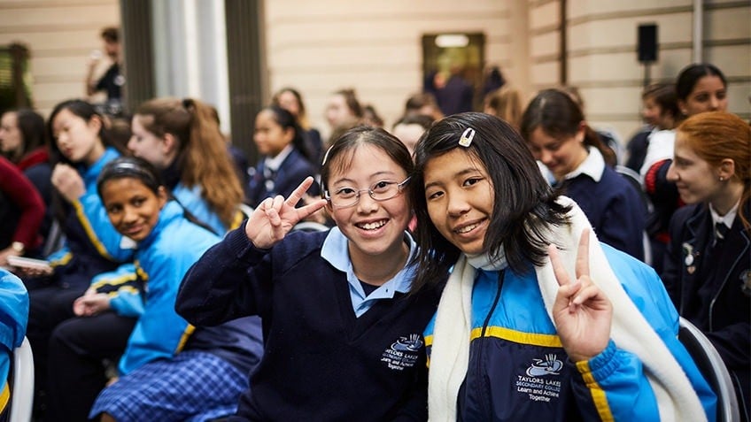 Two girls in school uniform smile and throw peace signs with fingers