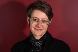 portait of woman with short hair and clear spectacles against red background