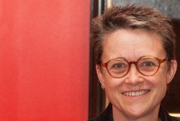 Kelly Gardiner Woman with short hair and spectacles against a red background