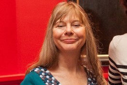 Dr Lucy Sussex woman with blonde hair and blue dress against a red background