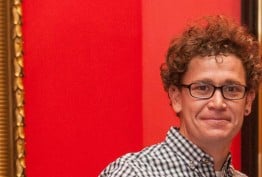 man with curly hair and glasses against a red background