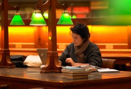 A high school student writes beneath a green desk light in a dim room