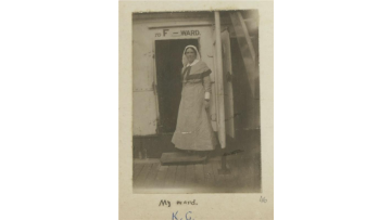 Black and white photograph of nurse Kathleen Gawler in uniform standing outside a doorway marked 'F Ward'