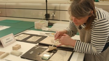 A woman with a scalpel gently prods some historic documents