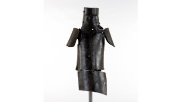 Photograph of Ned Kelly's suit of armour against a white/grey background. The armour has been installed on a metal pole.