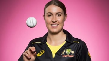 A woman spins a cricket ball against a pink backdrop