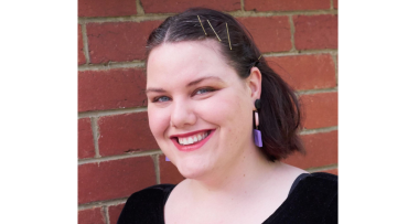 Author Clea Chiller smiling at the camera wearing purple, dangly earring and a black top.