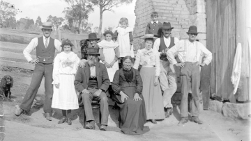 Black and white image showing a group of eleven people and two dogs, the people all smiling towards the camera.