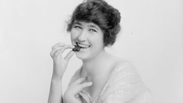 A woman smiles as she places a chocolate in her mouth