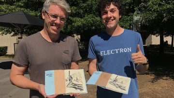 colour photo of two men in T-shirts holding books