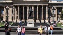 Colour photo of State Library Victoria front steps and portico, with statue of Redmond Barry and people walking down the steps