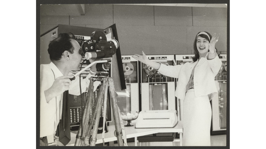 A black and white photo of a woman talking to a film camera