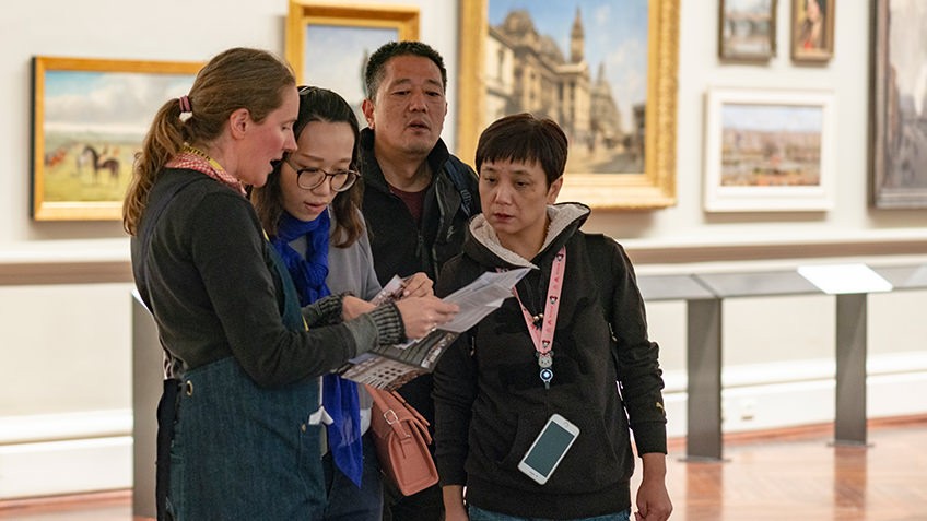 staff member helping visitors in artwork-lined Cowen Gallery