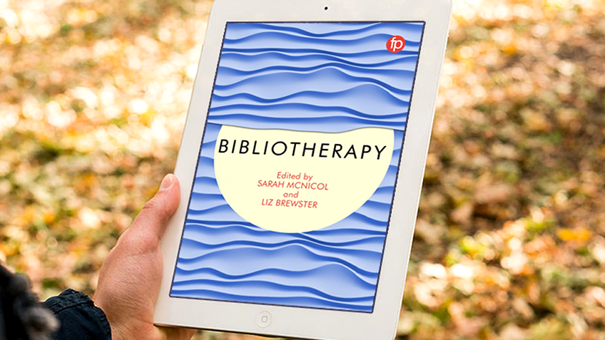 A hand holds an iPad against a background of autumn leaves