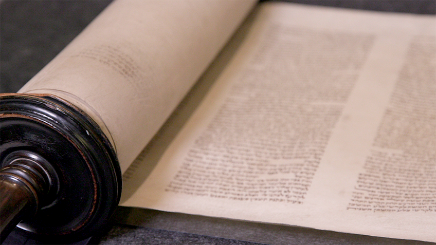A manuscript lays unfurled from its scroll