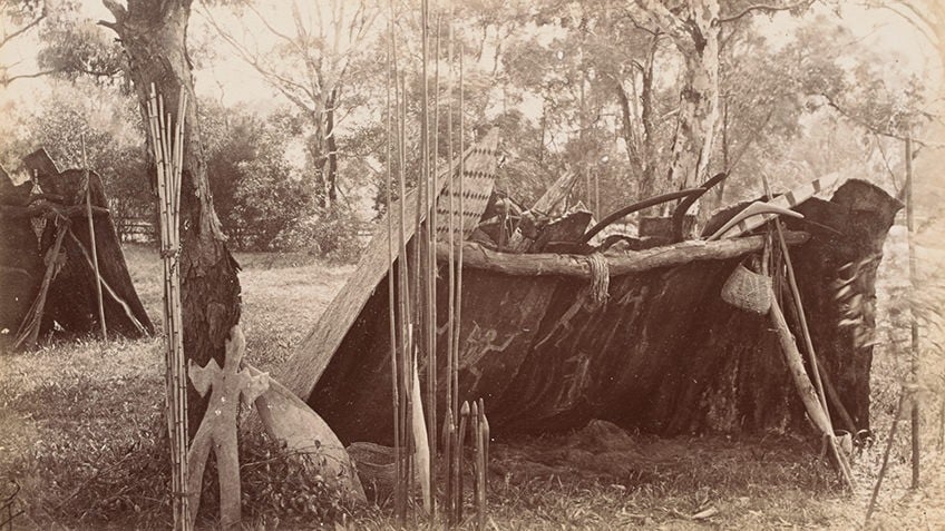 sepia photo of bark lean-to with Aboriginal tools, art and baskets