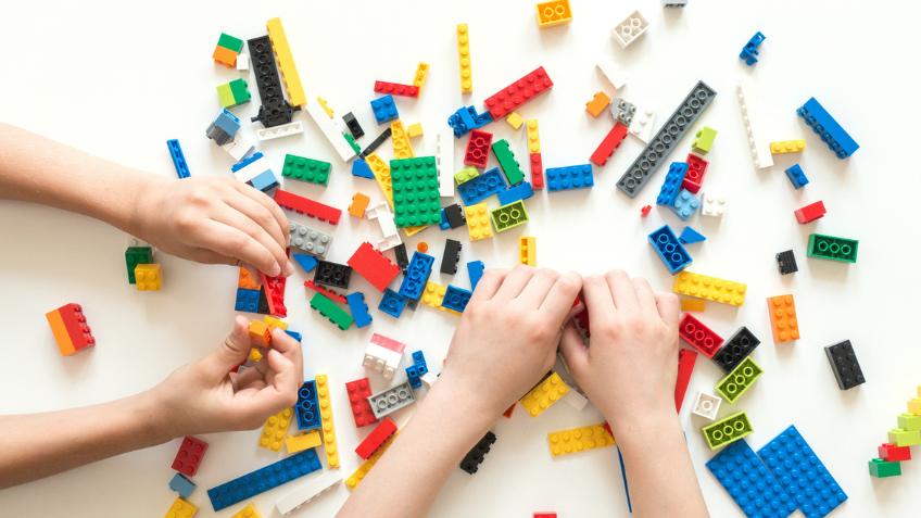 An image of two kids hands playing with colourful LEGO
