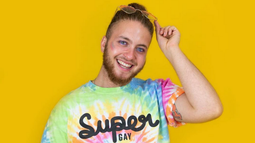 Headshot in front of a yellow background with a rainbow shirt