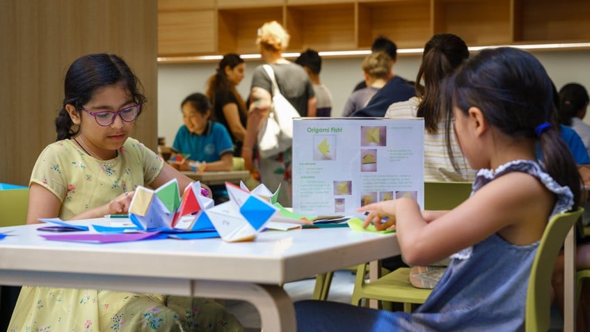 Young girls make paper origami at a table