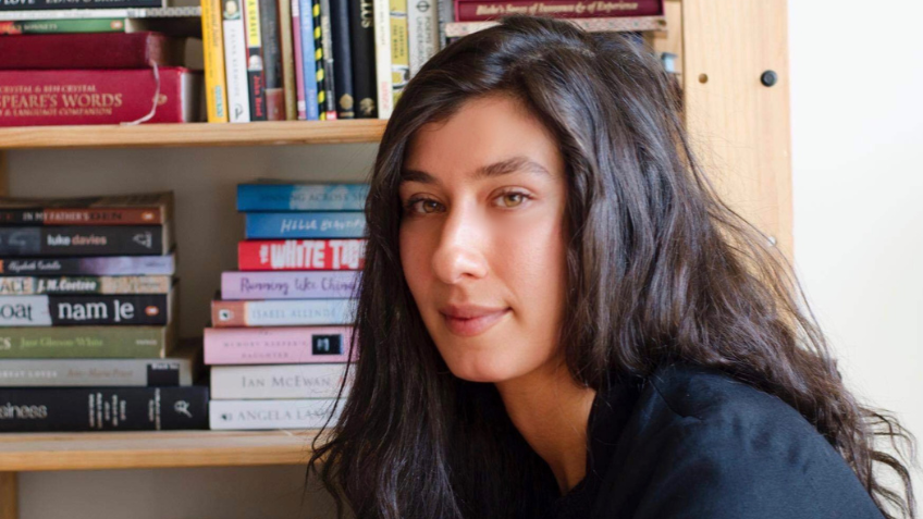Author Didem Caia staring at the camera with a book shelf behind her. 