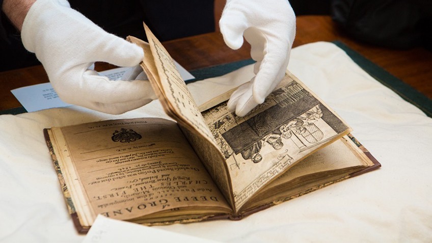 A pair of gloved hands turn the pages of a rare and valuable book