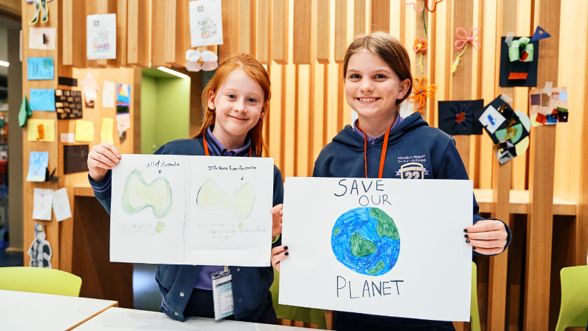 Two children holding up their artwork about the environment and saving our planet.