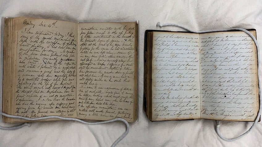 Two books lay open on a pillow, their pages filled with cursive handwriting