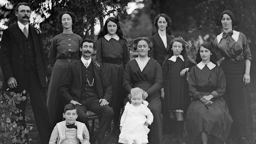 Black and white Edwardian portrait of a family group of 11 people, including parents, baby and children to young adults