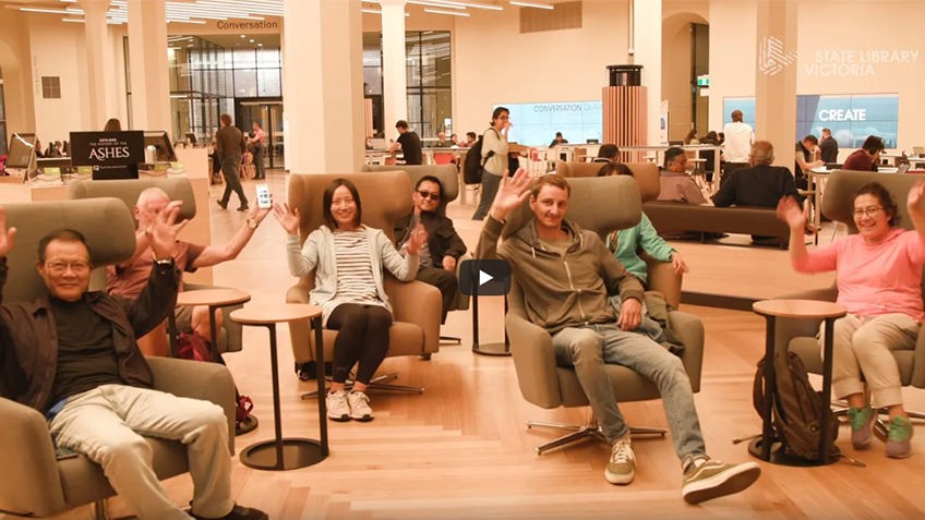 smiling people seated in public space waving at camera