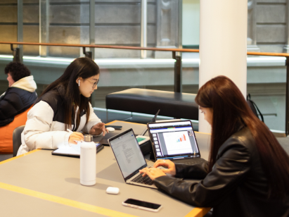 Two uni students studying with their notebooks and laptops on a mezzanine level of the Library