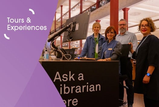 A group of four people smiling and standing behind a desk that has a sign saying 'Ask a Librarian' on it