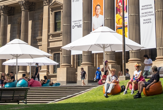 Library forecourt with umbrellas and people talking and reading books