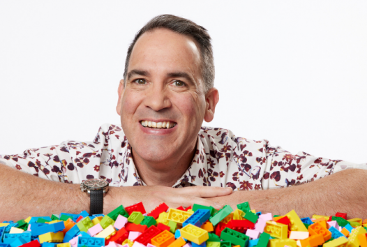 Ryan McNaught - The Brickman - leaning over a pile of colourful LEGO bricks