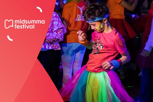 Boy wearing bandanna, pink shirt and ranbow tulle skirt is mid-dance