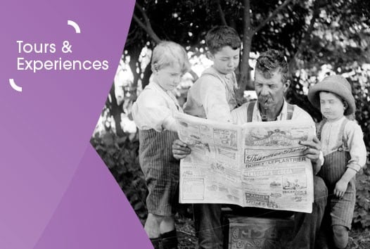 Black and white photograph of an adult man reading a newspaper with three children next to him. They are outside, and there are bushes and trees behind them. On the left is a purple graphic overlay with white text that says tours and experiences.