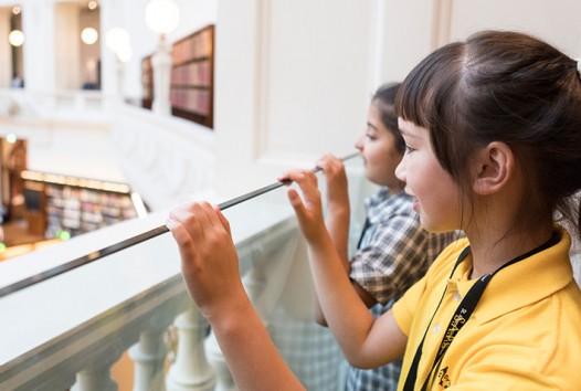 schoolgirls peering over the ornate balcony of a Dome Gallery in the octagonal La Trobe Reading Room