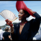 A black woman in black dress and blight red hat, smiling and waving her white fan