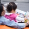 A baby being held by her mother whilst holding a picture book and turning the pages.